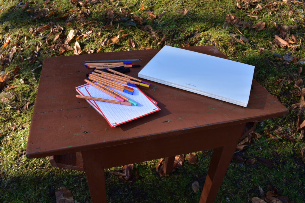 Ordinateur portable et carnets posés sur une table en bois en extérieur, illustrant une approche humaine et concrète