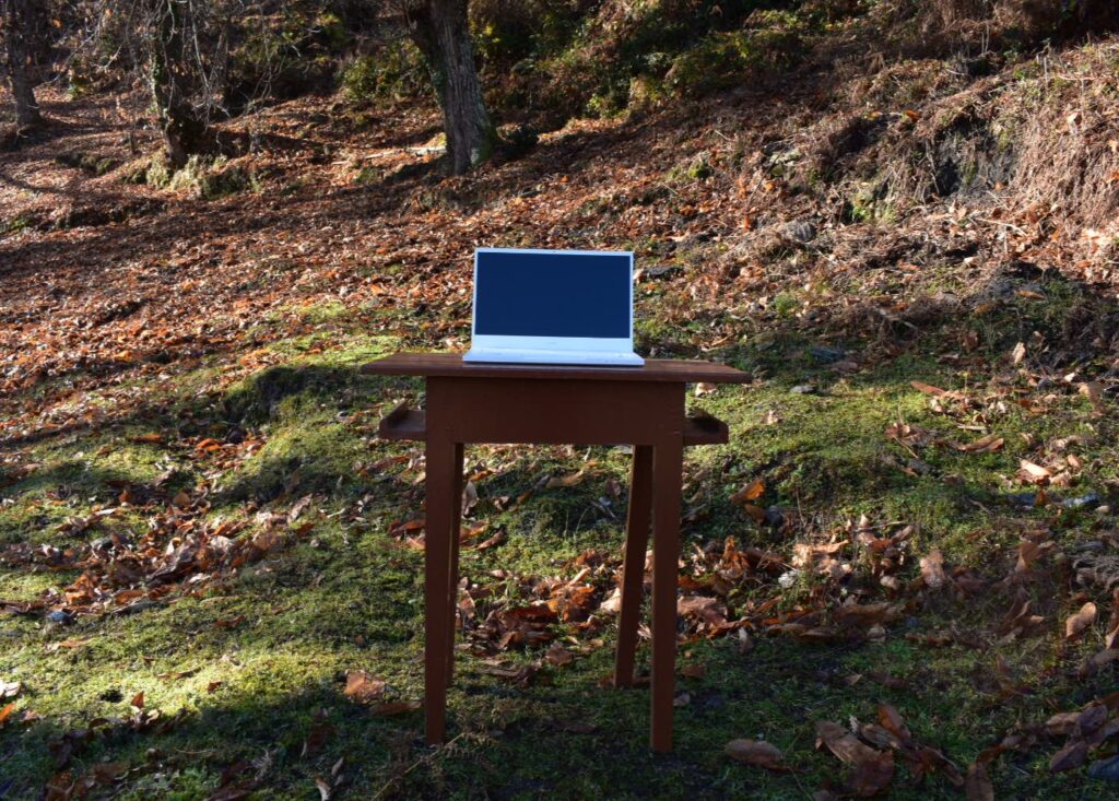 Ordinateur portable posé sur une table en bois en pleine nature, illustrant le travail digital ancré sur le terrain
