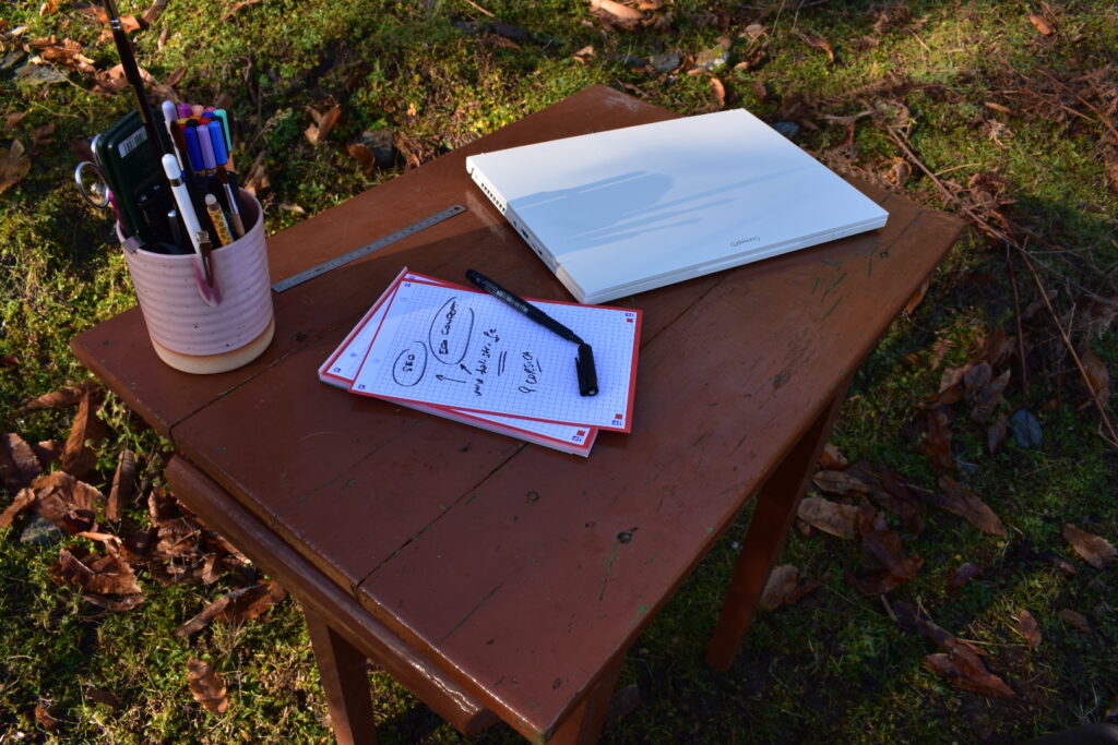 Carnet et matériel de travail posés sur une table en bois en extérieur, illustrant une approche simple et concrète